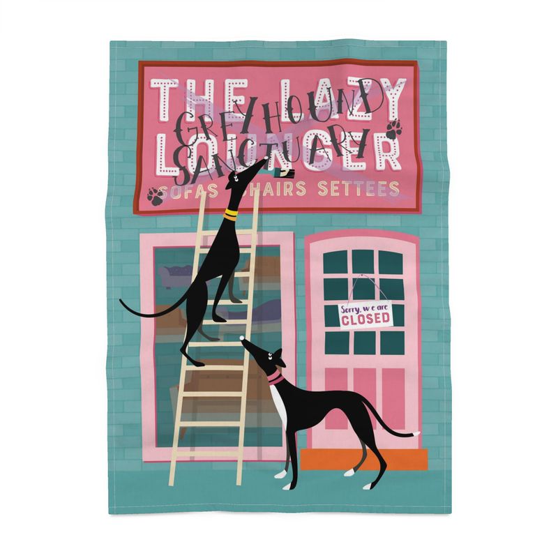 A tea towel with a turquoise background. It has an image of the shop front of a sofa shop called the Lazy Lounger. The shop is closed. There is a greyhound on a ladder with a paintbrush in their mouth. They are painting Greyhound Sanctury over the top of the shop sign. A 2nd greyhound is watching from the ground.