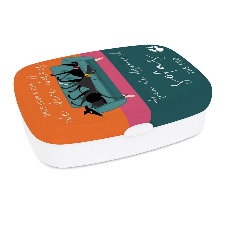 A lunch box. The base is white. The top has a full colour print wrapped around the sides. The background colour on the lid is turquoise, pink & orange. On the lid is an illustration of 3 greyhounds on a 2 seat teal sofa. Around the illustration the text reads; Once upon a time we were wolves. Then we discovered sofas. The End.