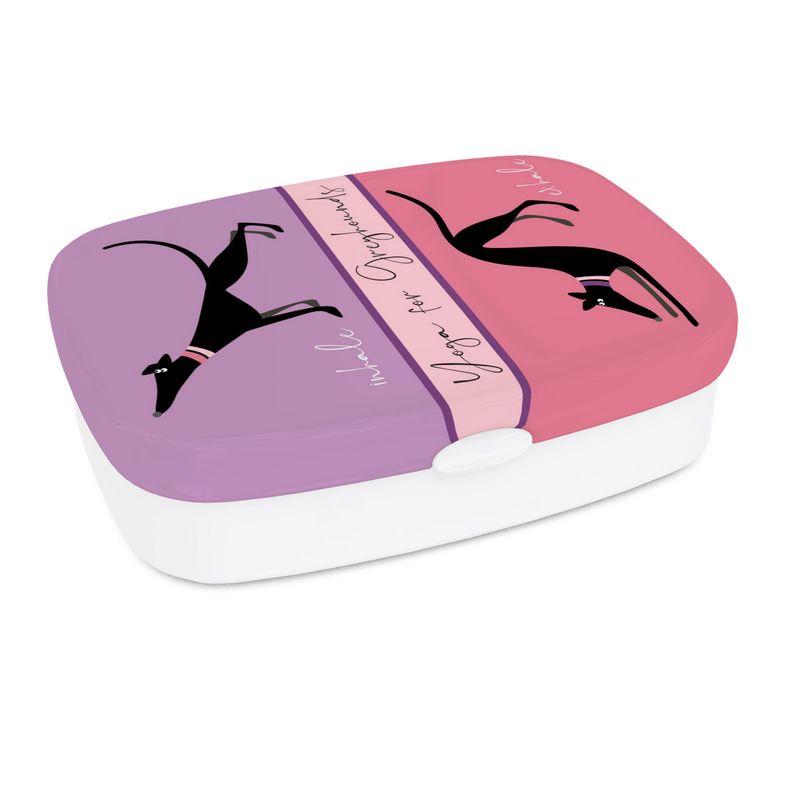 A lunch box white white base. The top has a full colour print. The top section is lilac and features a image of a cute black greyhound stretching it's front legs and nose up, it's back legs stretched behind. The text reads 'Inhale'. The lower image is on pink and shows a black greyhound with it's front legs and head in a bowed and back legs straight, tail in the air. The text reads exhale. Text in the middle of the box reads 'Yoga for Greyhounds'.