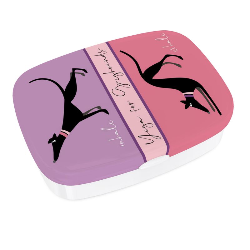 Different view of lunch box. The top has a full colour print. The top section is lilac and features a image of a cute black greyhound stretching it's front legs and nose up, it's back legs stretched behind. The text reads 'Inhale'. The lower image is on pink and shows a black greyhound with it's front legs and head in a bowed and back legs straight, tail in the air. The text reads exhale. Text in the middle of the box reads 'Yoga for Greyhounds'.